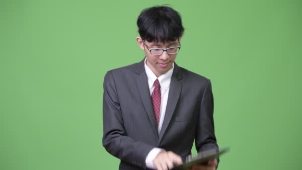 Jovem empresário asiático lendo com prancheta e ombros encolhendo — Vídeo de Stock