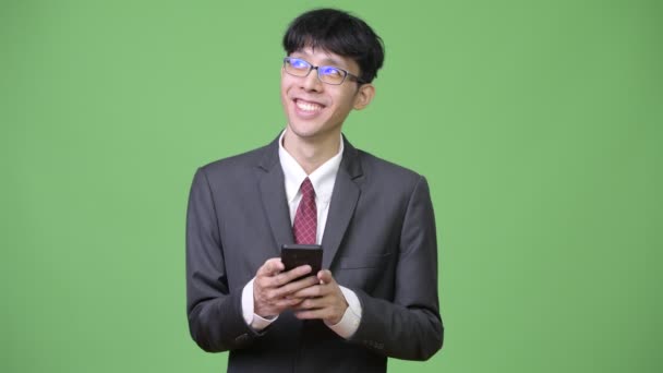 Young happy Asian businessman thinking while using phone — Stock Video