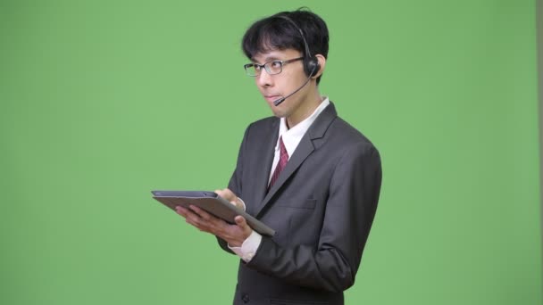 Young Asian businessman using digital tablet while working as call center representative — Stock Video