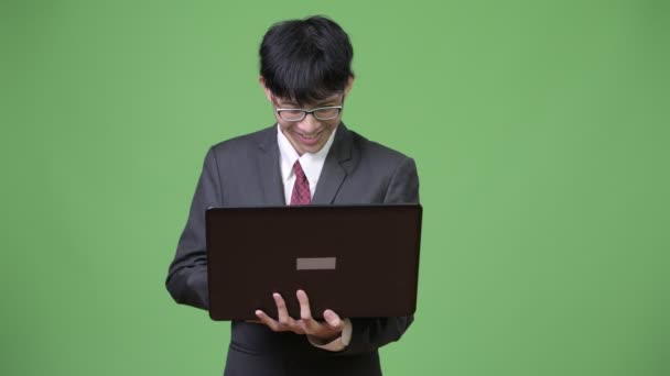 Young happy Asian businessman smiling while using laptop — Stock Video