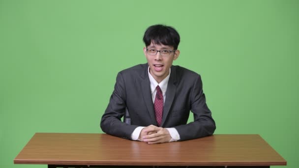 Young Asian businessman as newscaster talking and presenting something at the back — Stock Video