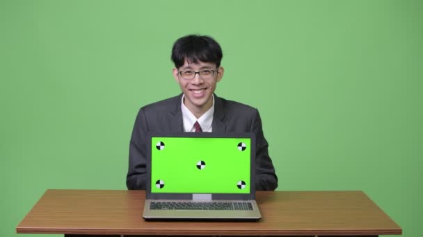 Jovem feliz empresário asiático sorrindo ao mostrar laptop para câmera — Vídeo de Stock