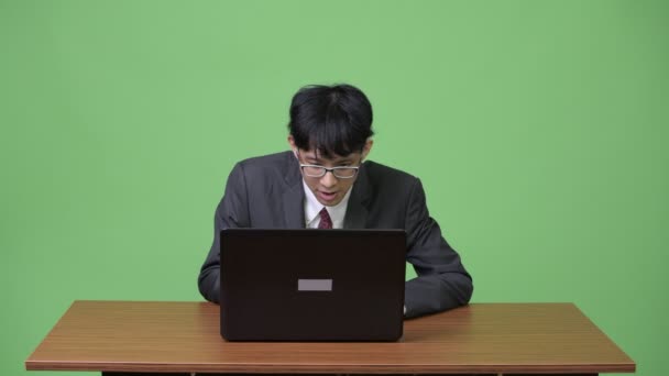 Молодой счастливый азиатский бизнесмен использует ноутбук и получает хорошие новости — стоковое видео