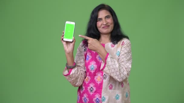 Mature happy beautiful Indian woman showing phone and pointing finger — Stock Video