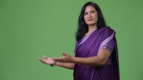 Dojrzałe szczęśliwy piękny Indian kobieta pokazując coś z tyłu sobie tradycyjne stroje Sari — Wideo stockowe