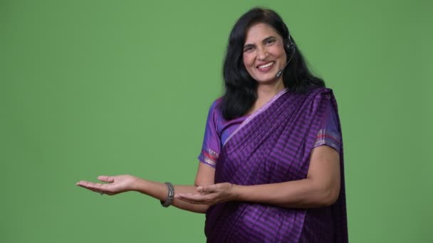 Mogen glad vacker indisk kvinna som call center representativa ler medan visar något — Stockvideo