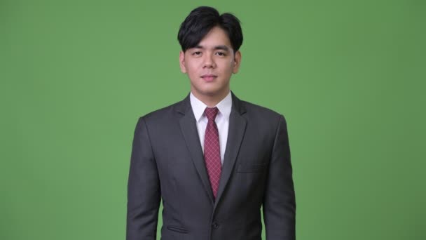 Gelukkig jonge knappe Aziatische zakenman glimlachend tegen groene achtergrond — Stockvideo