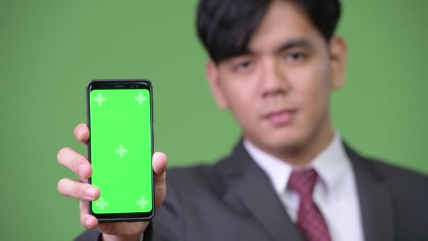 Jonge knappe Aziatische zakenman tonen mobiele telefoon — Stockvideo