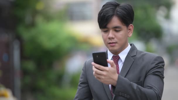 Young handsome Asian businessman using phone in the streets outdoors — Stock Video