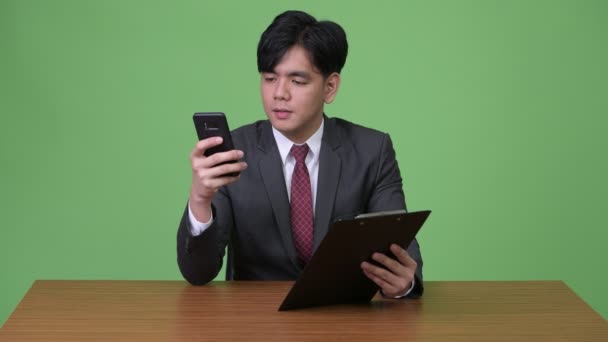 Ung Vacker asiatisk affärsman arbetar med Urklipp mot grön bakgrund — Stockvideo