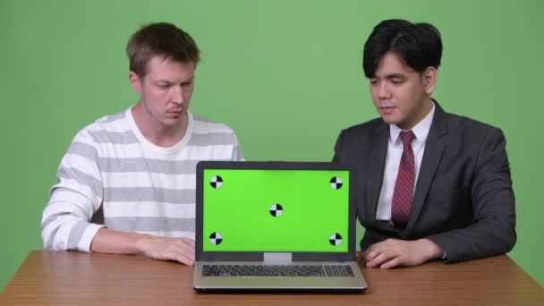 Молодой азиатский бизнесмен и молодой скандинавский бизнесмен работают вместе с ноутбуком — стоковое видео
