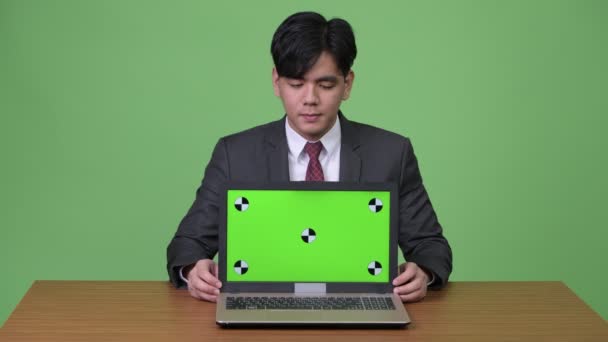 녹색 배경에 노트북을 보여주는 젊은 잘생긴 아시아 사업가 — 비디오
