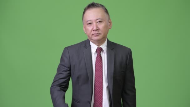 Dojrzałe zmęczony japoński biznesmen dając uścisk dłoni na zielonym tle — Wideo stockowe