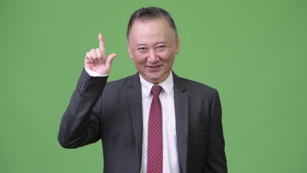 Mature happy Japanese businessman pointing finger up — Stock Video