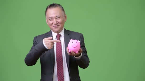 Rijpe Japanse zakenman holding piggy bank — Stockvideo