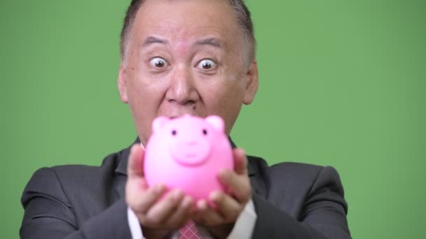 Mature Japanese businessman holding piggy bank — Stock Video