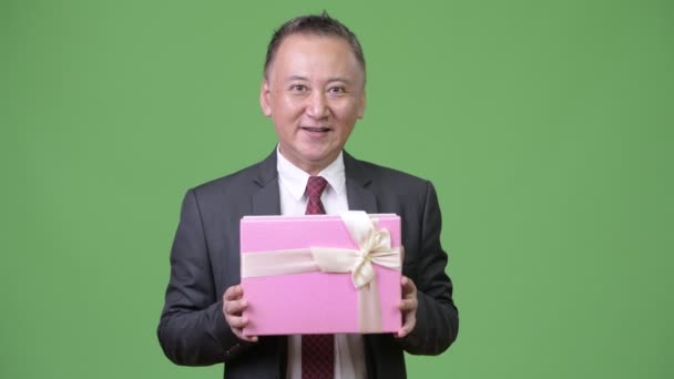 Mature Japanese businessman with gift box against green background — Stock Video