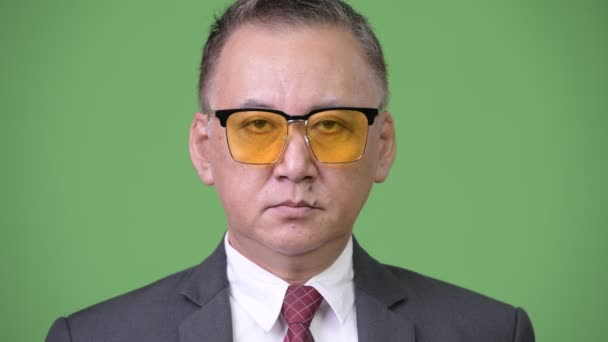 Зрелый японский бизнесмен в солнечных очках на зеленом фоне — стоковое видео