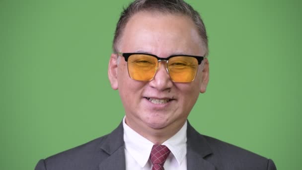 Зрілі японський бізнесмен носити сонцезахисні окуляри на зеленому тлі — стокове відео