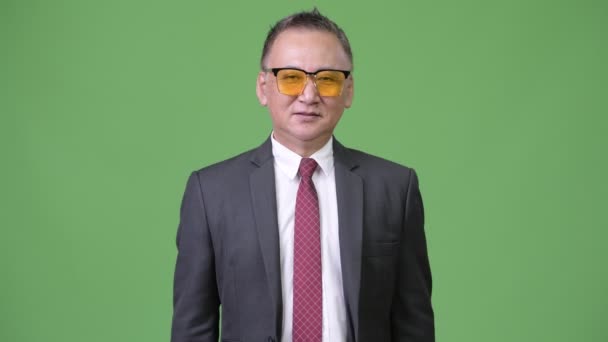Mature Japanese businessman wearing sunglasses against green background — Stock Video
