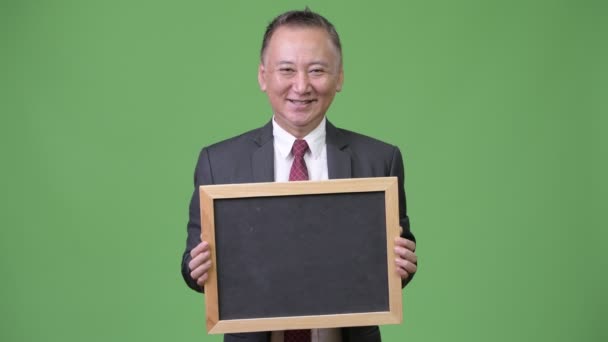 Starší japonský obchodník drží tabuli před zeleným pozadím — Stock video