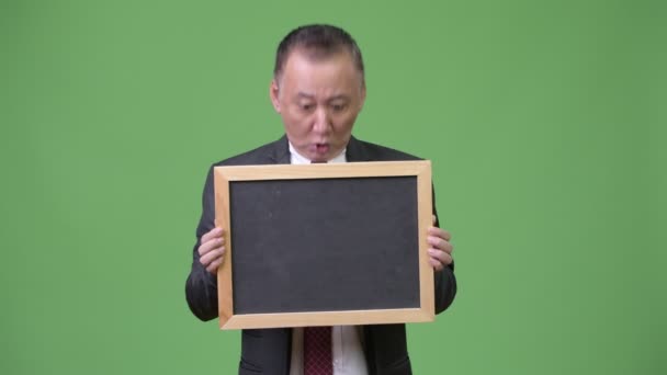 Ώριμη ιαπωνική επιχειρηματίας κρατώντας μαυροπίνακα ενάντια σε πράσινο φόντο — Αρχείο Βίντεο