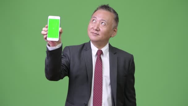 Зрелый японский бизнесмен показывает телефон на камеру — стоковое видео
