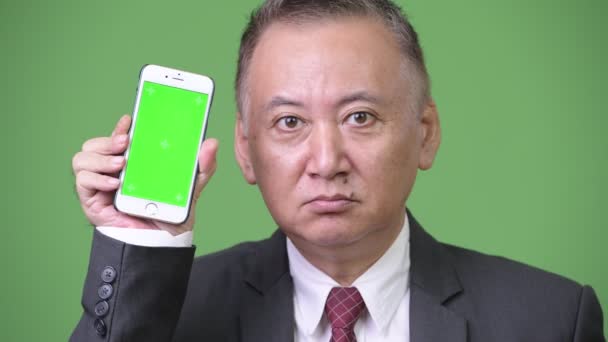 成熟的日本商人显示电话到照相机 — 图库视频影像