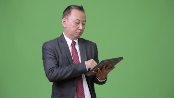Зрелый японский бизнесмен, работающий с цифровыми планшетами — стоковое видео