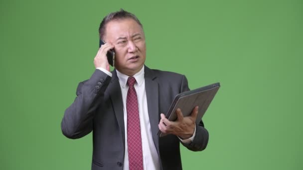 Зрелый японский бизнесмен, работающий с цифровым планшетом и телефоном — стоковое видео