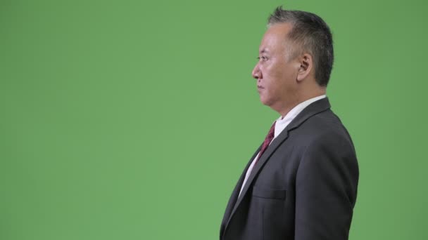 Перегляд профілю зрілих японського бізнесмена проти зелений фон — стокове відео