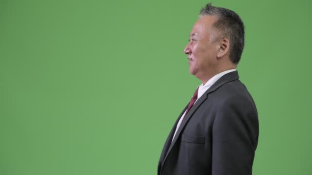 Profile view of mature Japanese businessman smiling against green background — Stock Video