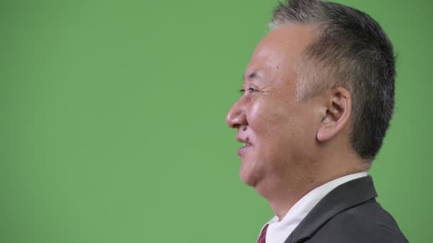 Перегляд профілю зрілих японського бізнесмена, посміхаючись на зеленому тлі — стокове відео