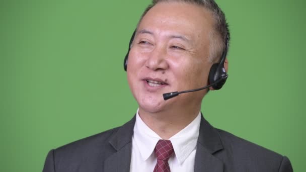 Japanischer Geschäftsmann arbeitet als Callcenter-Vertreter vor grünem Hintergrund — Stockvideo