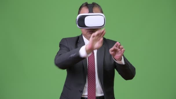 Зрелый японский бизнесмен, использующий гарнитуру виртуальной реальности на зеленом фоне — стоковое видео