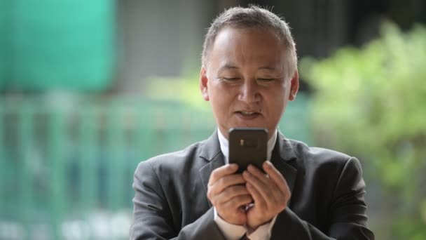 Dojrzały japoński biznesmen przy użyciu telefonu na ulicach, na zewnątrz — Wideo stockowe