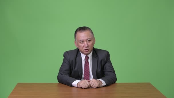 Mature Japanese businessman talking against green background — Stock Video