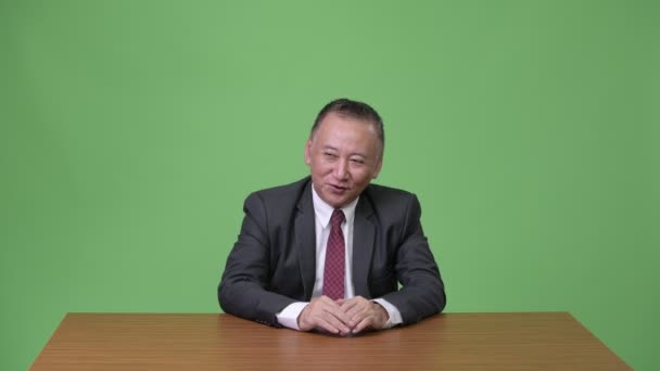 Rijpe Japanse zakenman praten tegen een groene achtergrond — Stockvideo