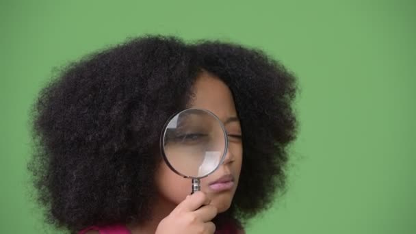 Молодая симпатичная африканская девушка с африканскими волосами, использующая увеличительное стекло — стоковое видео