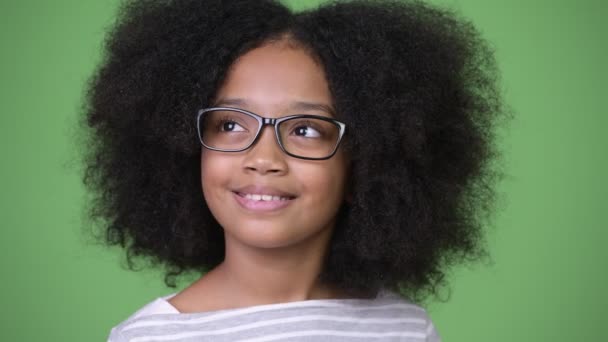 Joven chica africana feliz con el pelo afro sonriendo y pensando en fondo verde — Vídeo de stock