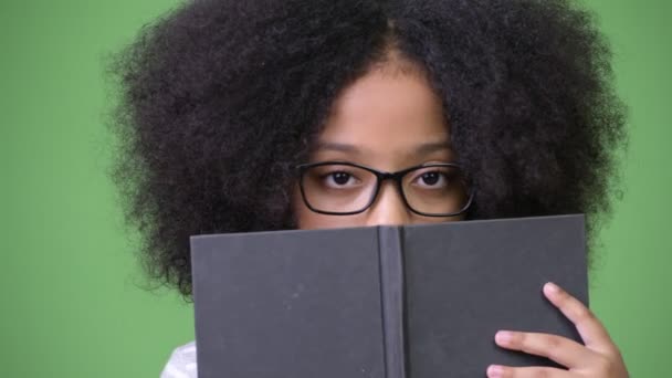 Young cute African girl with Afro hair studying against green background — Stock Video