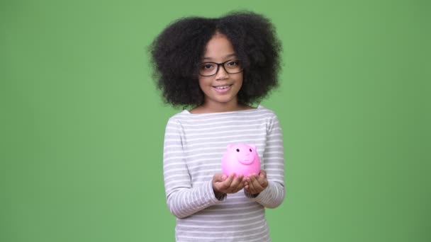 Jovem menina africana bonito com cabelo afro segurando porquinho banco — Vídeo de Stock