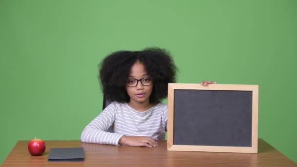 Junge süße afrikanische Mädchen mit Afro-Haar zeigt Tafel im Sitzen — Stockvideo