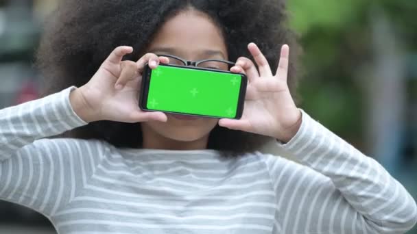 Jeune fille africaine mignonne avec des cheveux afro montrant téléphone dans les rues à l'extérieur — Video