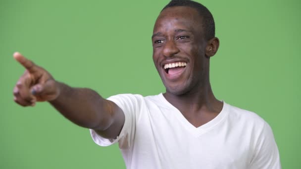 Joven hombre africano feliz sonriendo mientras señala con el dedo a la distancia — Vídeo de stock
