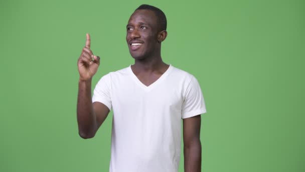 Jeune homme africain heureux souriant et pensant tout en pointant vers le haut — Video