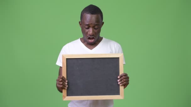 Молодой африканский мужчина показывает доску и выглядит шокированным — стоковое видео
