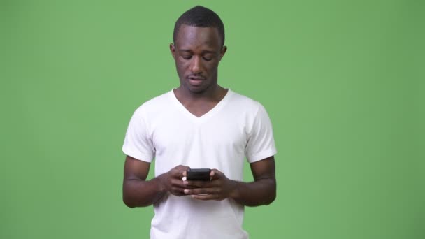 Junger Afrikaner benutzt Handy vor grünem Hintergrund — Stockvideo