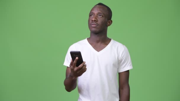 Giovane uomo africano pensando mentre si utilizza il telefono sullo sfondo verde — Video Stock