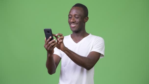 Afrikaanse jongeman met behulp van de telefoon tegen een groene achtergrond — Stockvideo